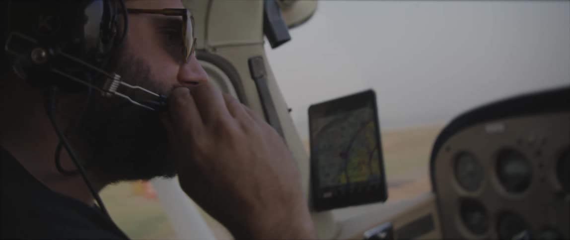 A man with a headset and sunglasses sitting in a vehicle with the sky and clouds in the background