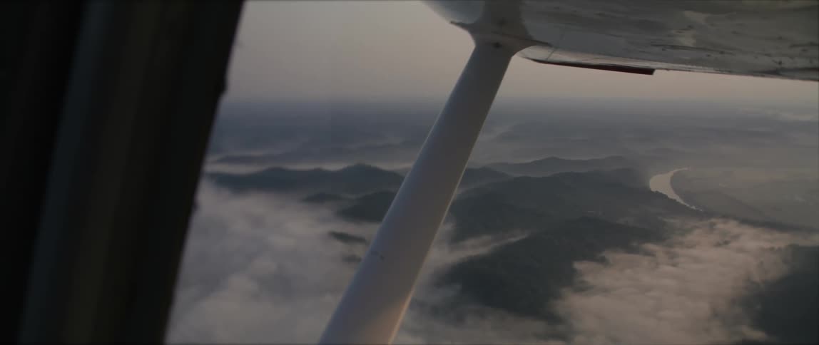 Small airplane flies over the clouds and the mountains