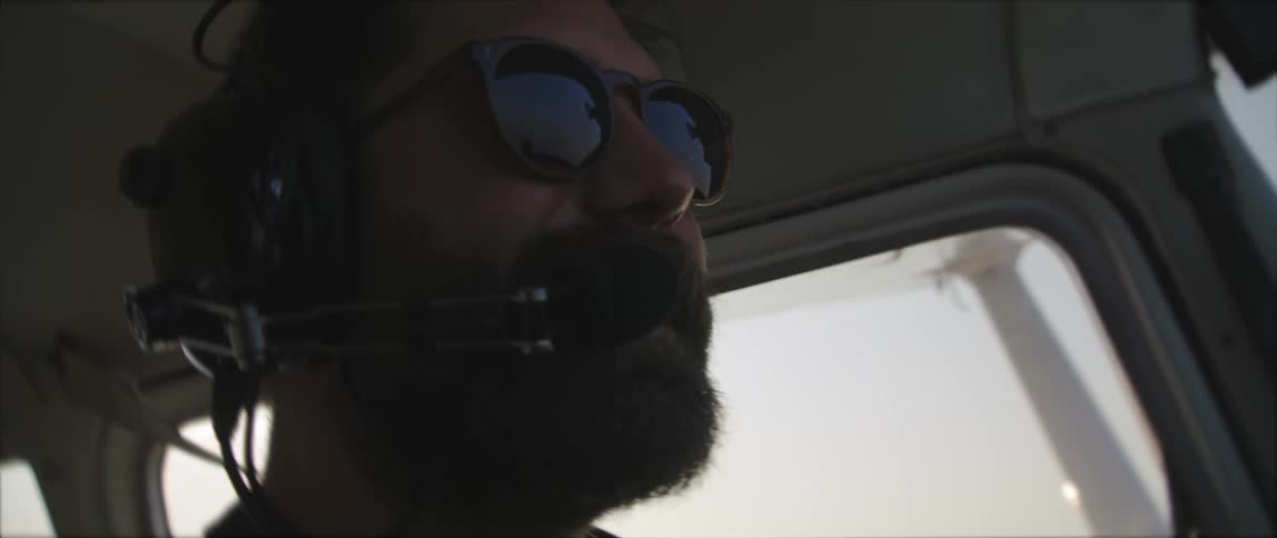 Male pilot with a beard sunglasses and an aviation headset operates the single engine plane