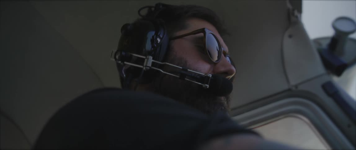 Male pilot with a beard sunglasses and aviation headset operates the single engine plane