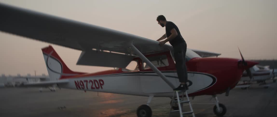 A man stands on a ladder working on a small airplane