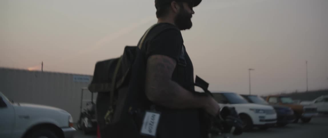 Photographer carrying equipment on a parking lot at sunset