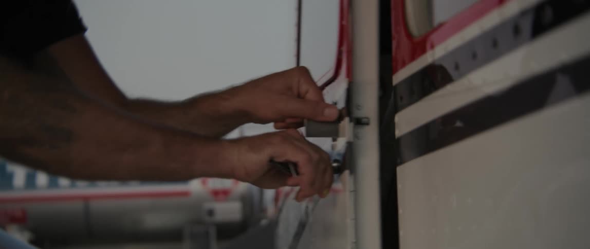 A person turns the handle of an airplane door and opens the door