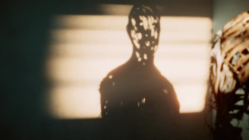 A sculpture shaped like a human but made out of wood and sticks casts a shadow on the wall behind it