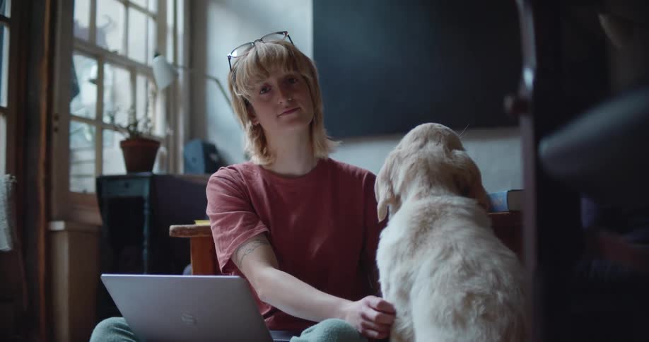 Woman sitting on the floor of the living room petting a dog while looking at the camera