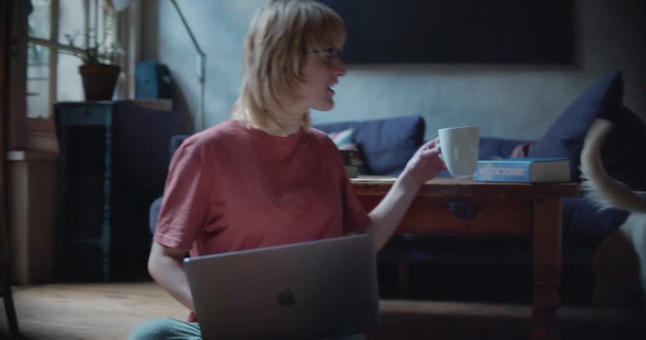 A woman with glasses sitting on the floor with a laptop and petting a dog