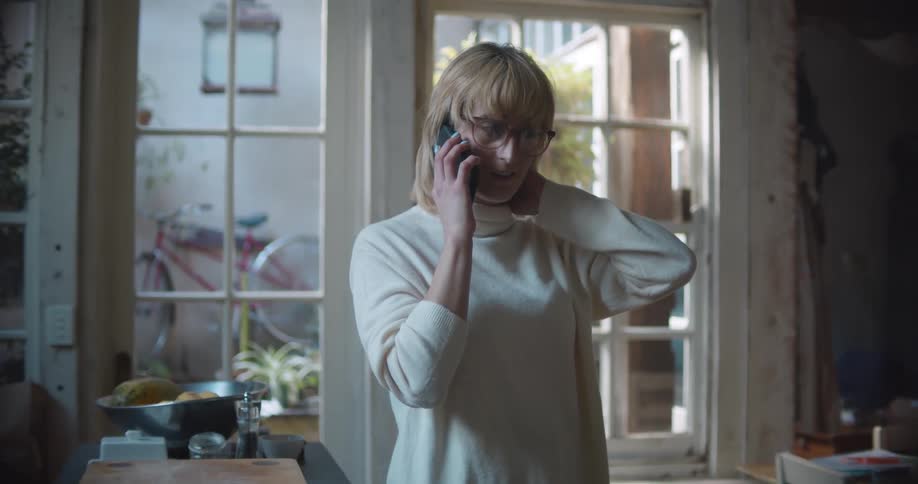 A woman with glasses in a room talking on a smart phone with a door in the background