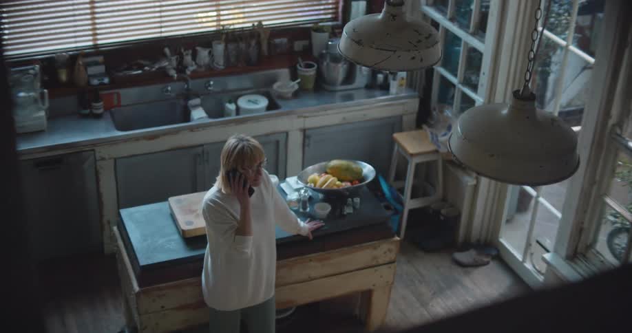 A woman stands in her rustic kitchen with one hand on the island as she talks on the phone