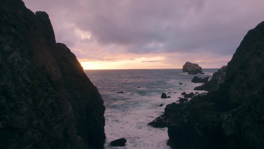 Waves are crashing at the base of cliffs at dusk