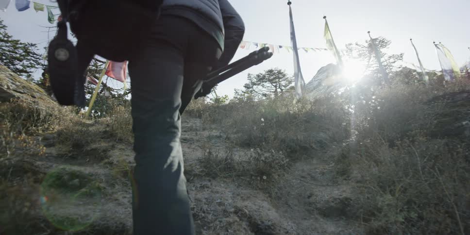 A photographer carries his equipment up a steep hill towards a monastery