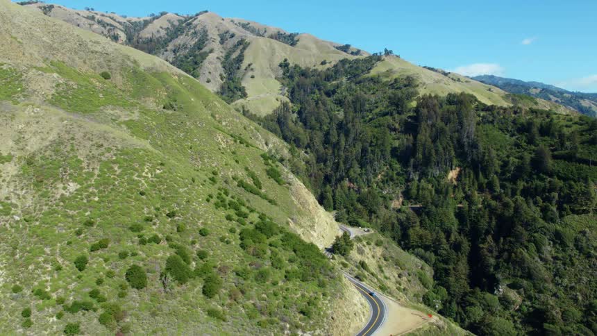 Vehicle drives on road winding through grassy mountains