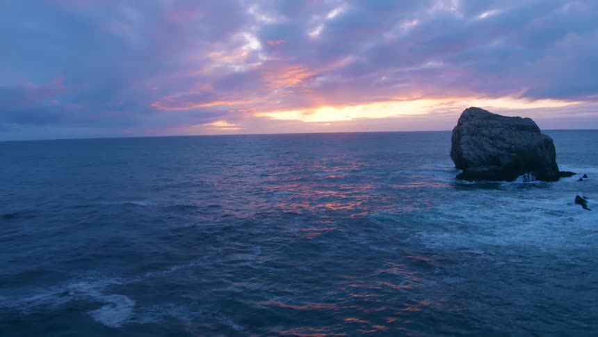 Jutting out of the choppy ocean waters several large rock formations line a coastal area on a cloudy day