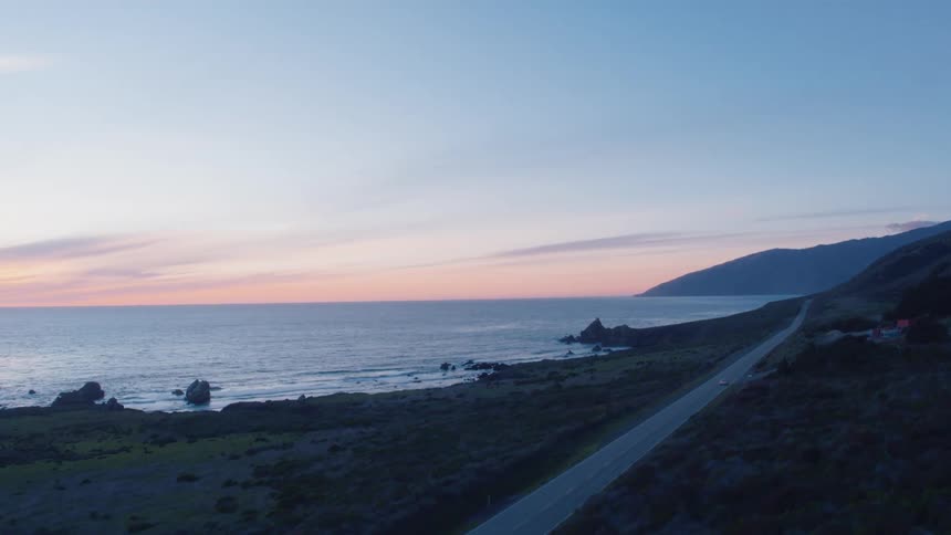 A car travels on a coastal road at sunset