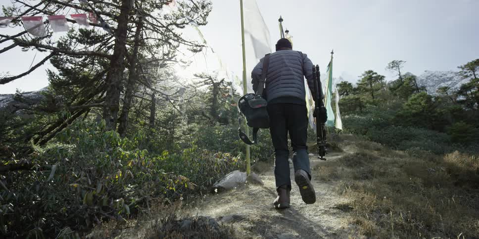 Person following an uphill trail carrying some equipment