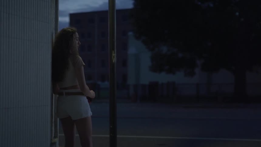 Woman with long hair stands on a street corner as cars travel by