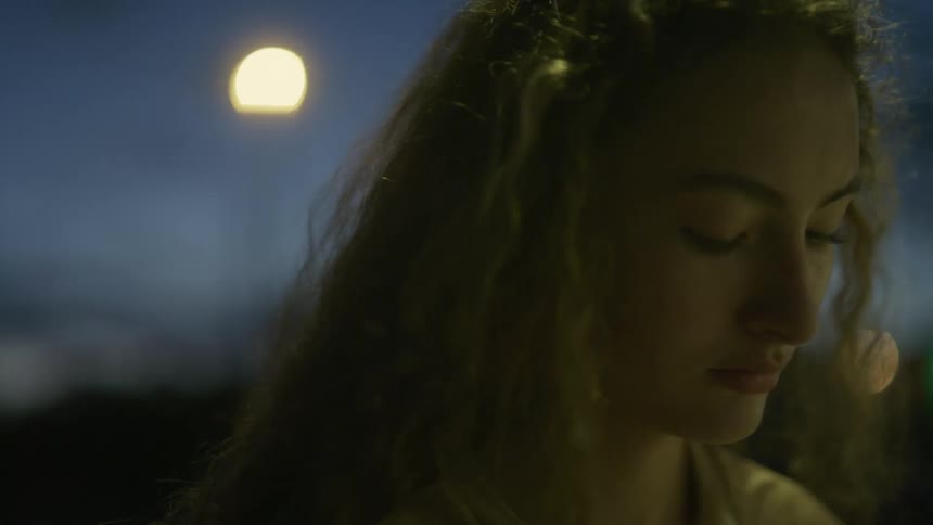 Wind blows through a womans long brown hair as she stands outside in a city at night