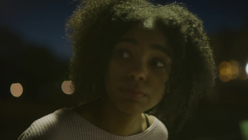 A young woman who is alone while outside at nighttime looks around nervously