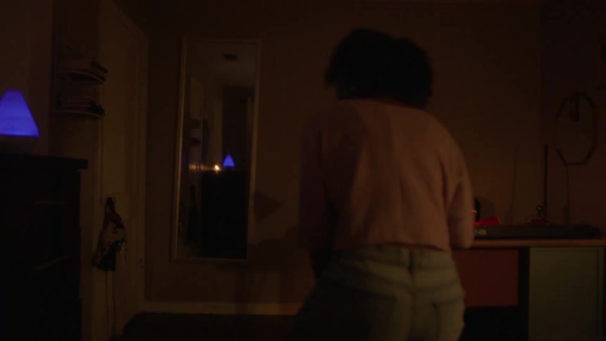 Woman walks into dimlylit room sitting on bed with mobile phone