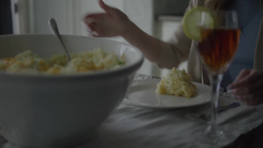 A female reaches out an serves herself a large spoonful of mashed potatoes