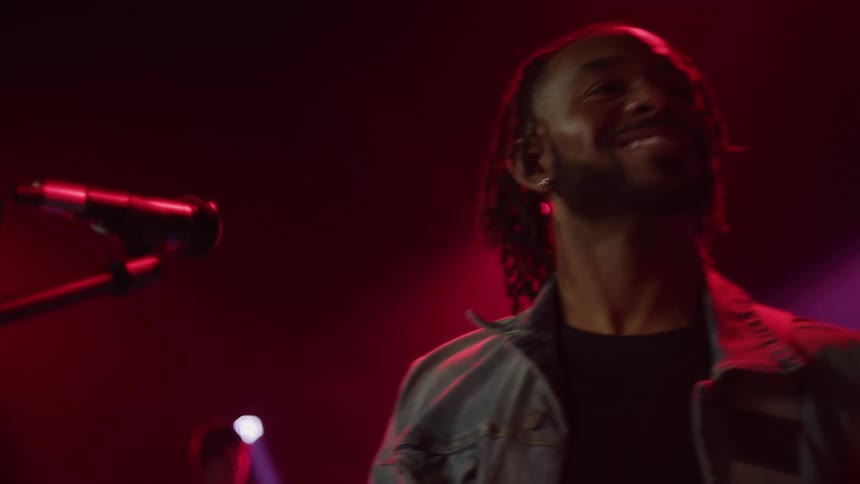 Guitarist performing with band on stage standing near microphone smiles and waves