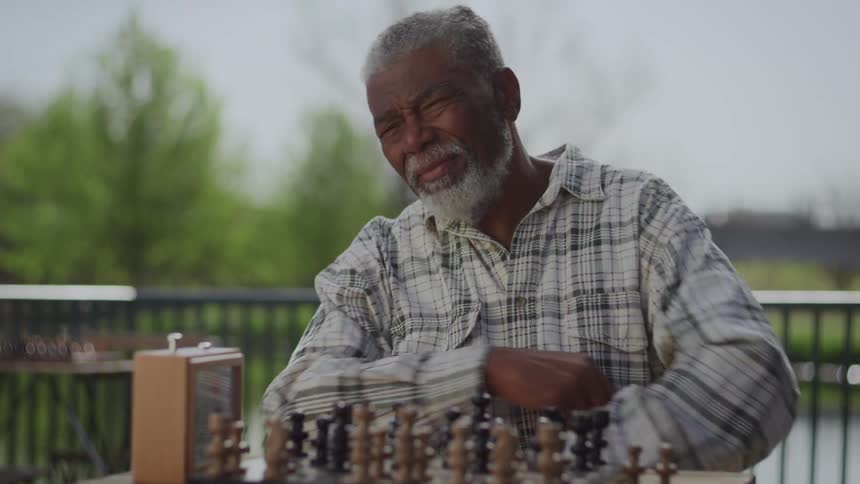 A man makes a move and captures a chess piece hits the clock and crosses his arms to wait