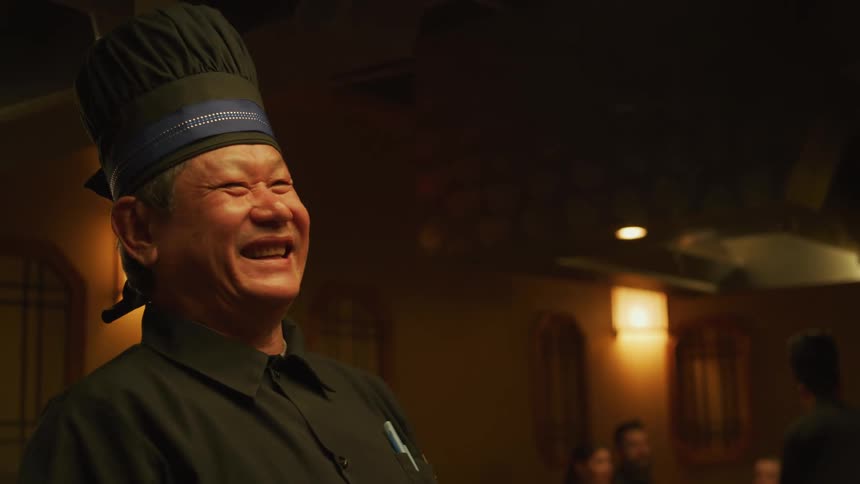 A chef at a hibachi restaurant laughs with customers