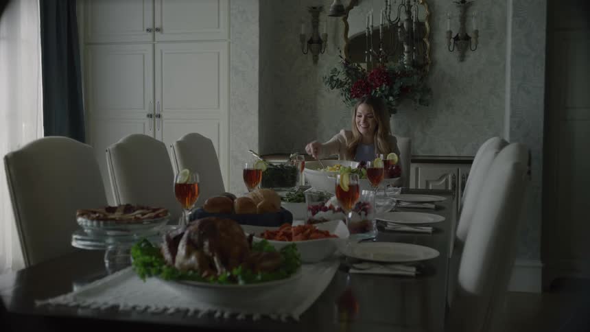 Woman sits at dining table spread with holiday meal talking to empty chairs