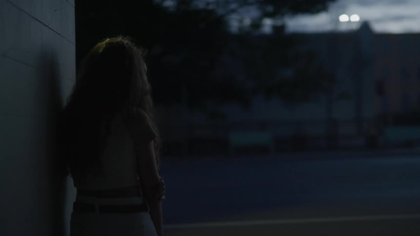 A woman stands by the side of a building as cars drive by