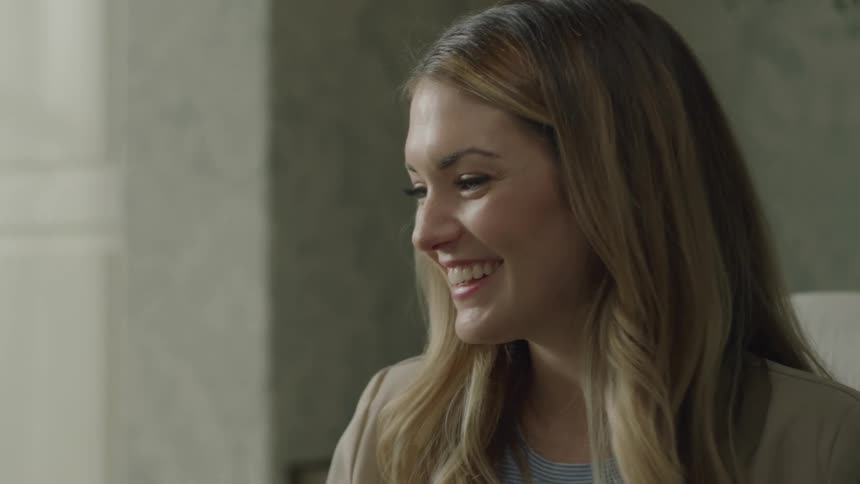 Blonde woman smiles and laughs as she sits in a chair