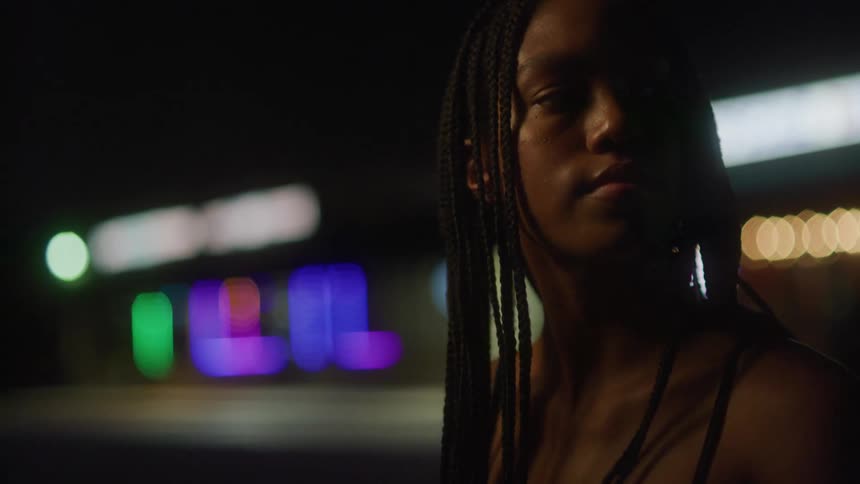 A young woman stands out front of a building with colorful flashing lights