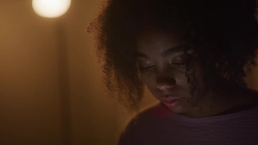 A woman with naturally curly hair looking down with a lamp light glowing behind