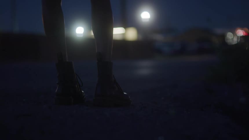 A woman pauses before slowly walking along the side of a road at night