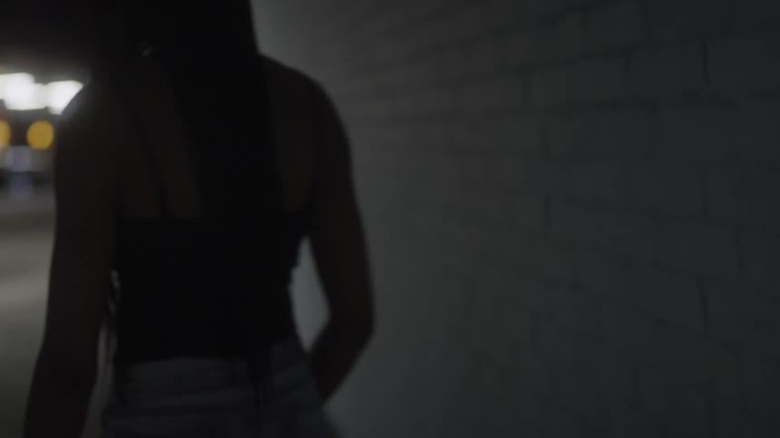 Black woman stands against a wall and looks at her cellphone then walks away