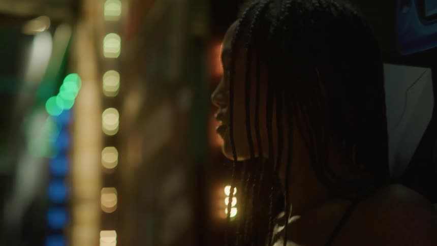 Black woman with long braided hair looks around while standing near flashing lights