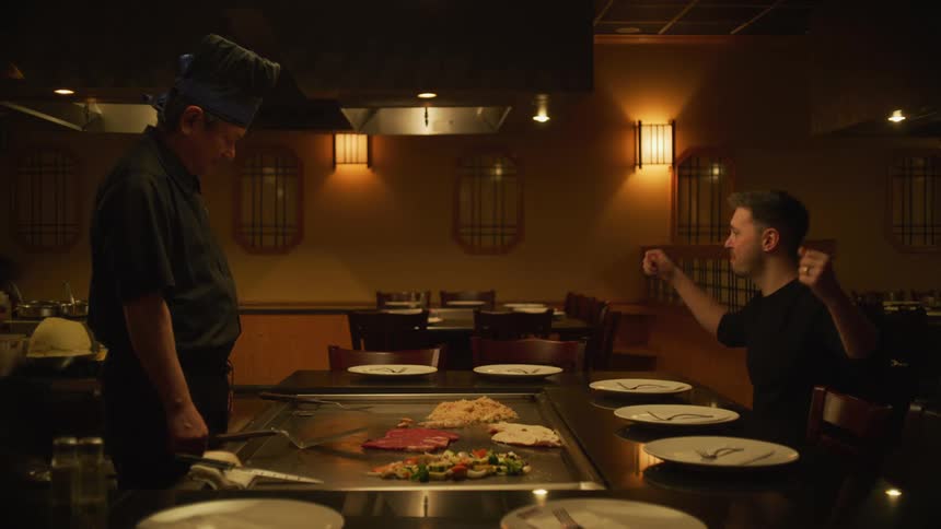 Man catches food thrown into air by chef and eats it celebrating briefly before realizing restaurant is empty