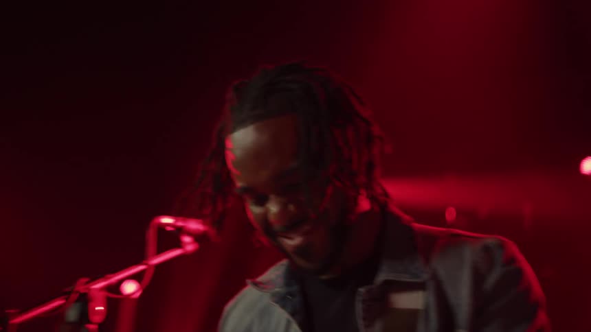 Band performs on stage smiling at each other under red stage lights