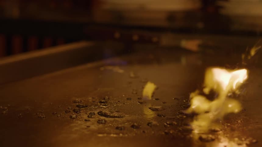 A person using a lighter fire lighter fluid a cloth and utensils to clean a grill