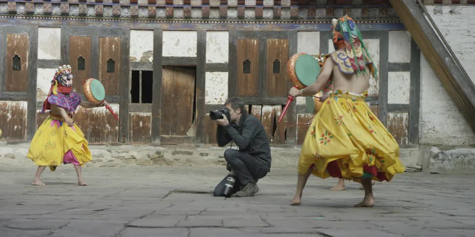 A man takes pictures of people in yellow skirts dancing