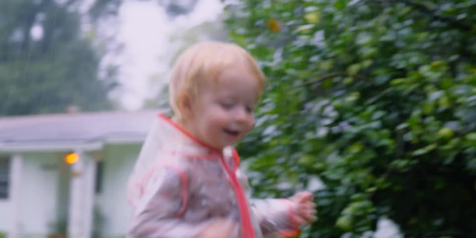 Young female toddler wearing a raincoat runs to her mother also in a raincoat and hugs her
