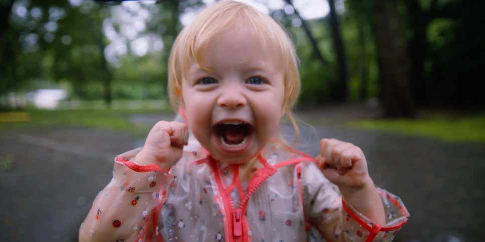 A little kid screams with joy as she is outside in rain wearing a raincoat