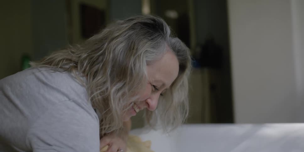 A woman with gray hair smiles at her grandchild who is taking a bath
