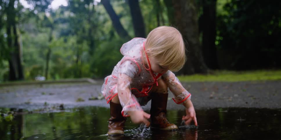 Toddler wearing a raincoat playing with a puddle of water outdoors