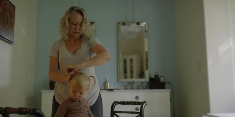 Mother puts daughters hair up in room across from twin wall mirrors