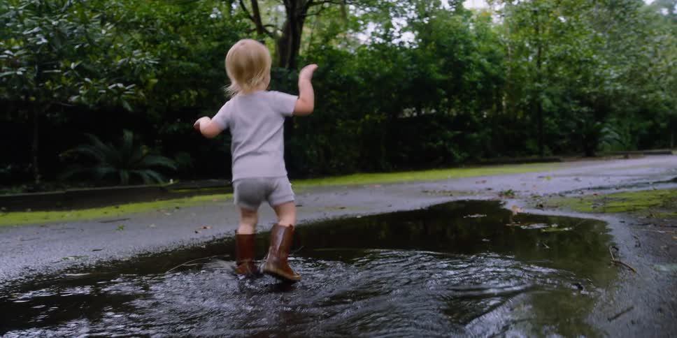 Toddler blonde girl with brown boots jumps in the puddle