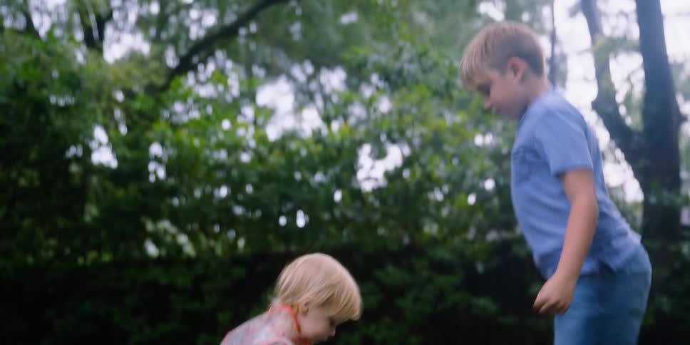 A boy spins in place while jumping up and down in a puddle alongside a younger girl