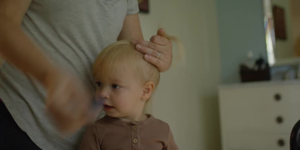 A mother combs her daughters hair into a pony tail and hands the comb to her daughter to hold