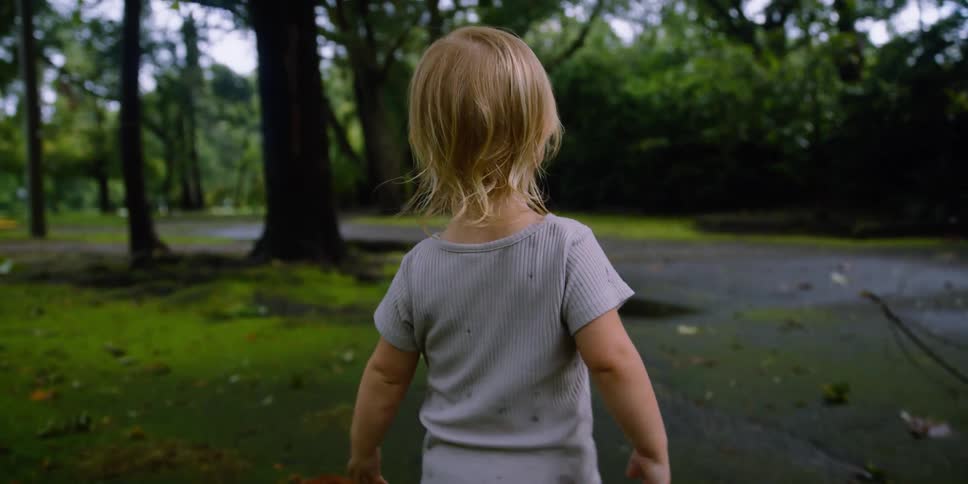 A little girl walking with trees vehicles the sky and clouds in the background