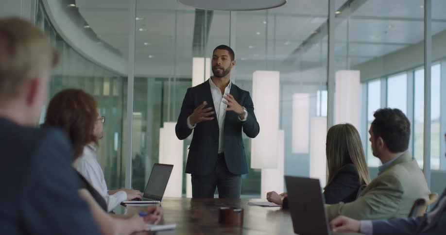 A man in a conference room talking to people sitting at a table with laptops