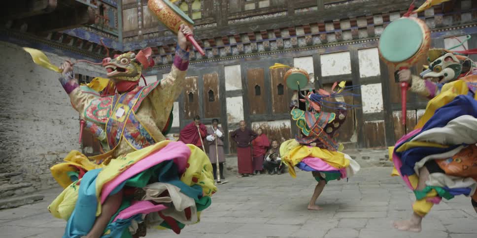 Monks in colorful attire and mask dance in an outdoor ceremony