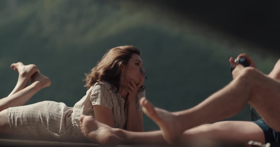 Woman poses lying down outdoors as man takes pictures with camera